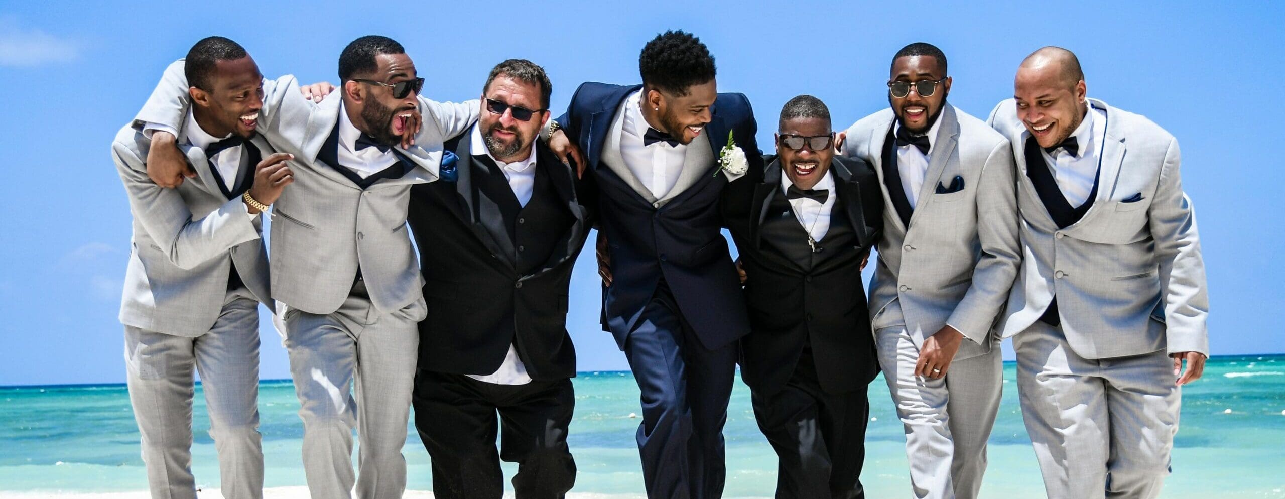 A group of men from a wedding party at the beach in suits